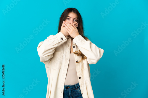 Young caucasian woman isolated on blue background covering mouth with hands