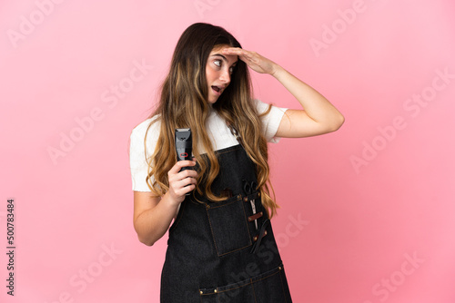 Young hairdresser woman isolated on pink background doing surprise gesture while looking to the side