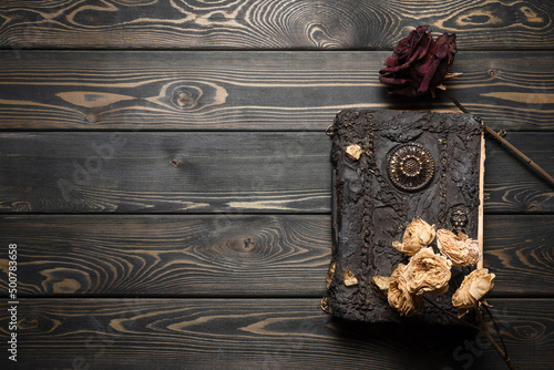 Ancient magic book and dry rose flowers on the old wooden table background with copy space. Witchcraft concept. photo