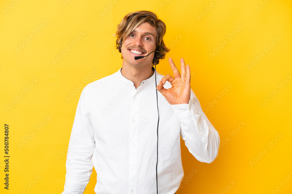 Telemarketer man working with a headset isolated on yellow background showing ok sign with fingers Telemarketer man working with a headset isolated on yellow background showing ok sign with fingers