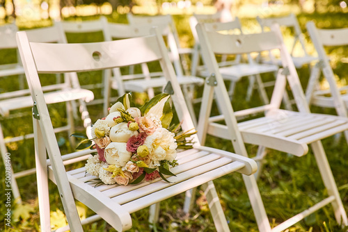 White chairs with a bouquet are in the park. A place for a wedding ceremony. Wedding decorations. Selective focus