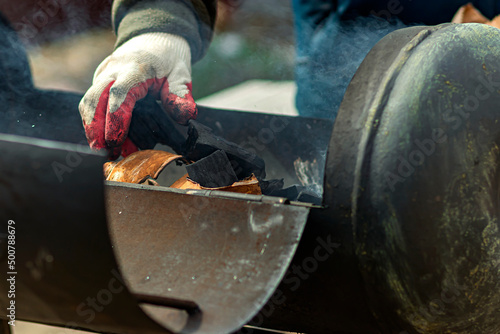 A man in a protective glove lays the bark of a tree to light the barbecue.