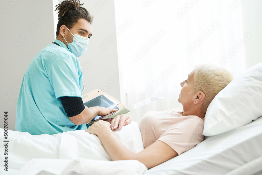 Doctor in mask sitting near patient in hospital bed Doctor in mask sitting near patient in hospital bed