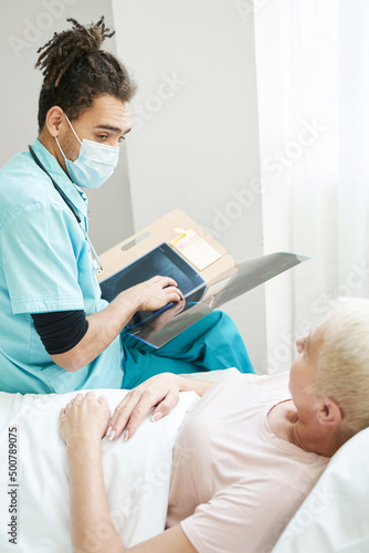 Young medic with x-ray staring at aged patient