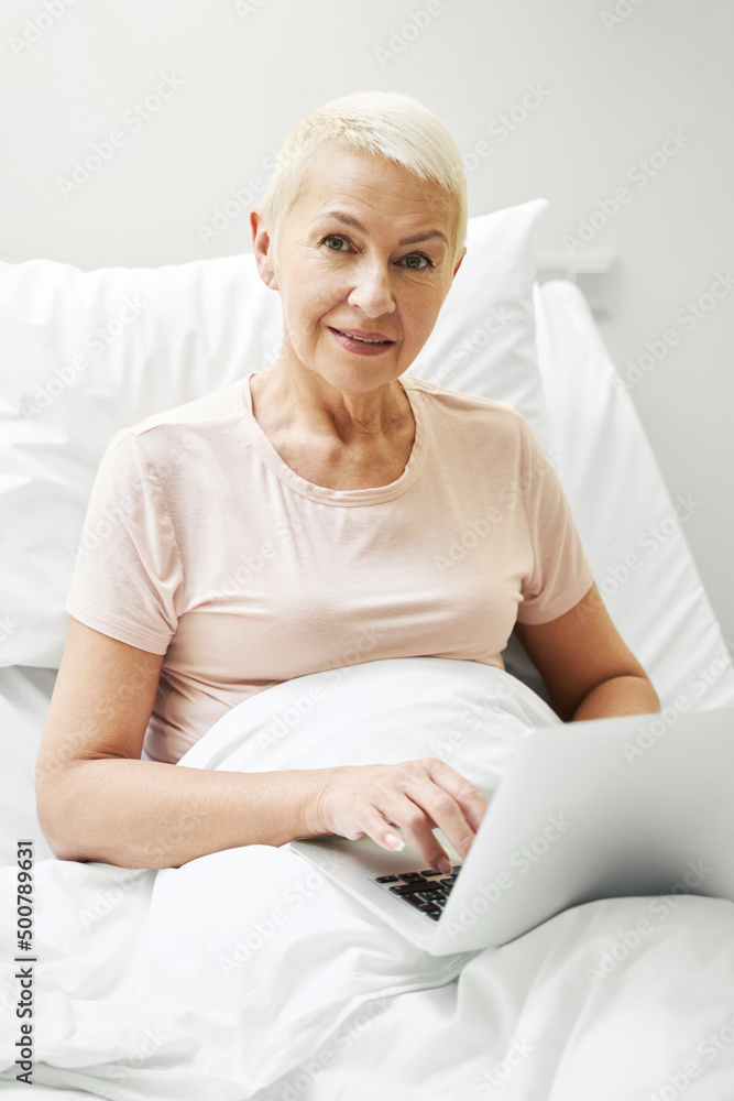 Aging person clicking on laptop in bed of medical center Aging person clicking on laptop in bed of medical center