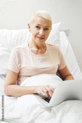 Aging person clicking on laptop in bed of medical center