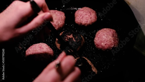 Woman turning over beef burger patties on a hot pan. Unhealthy burnt meat. Cooking homemade round minced meat cutlets.