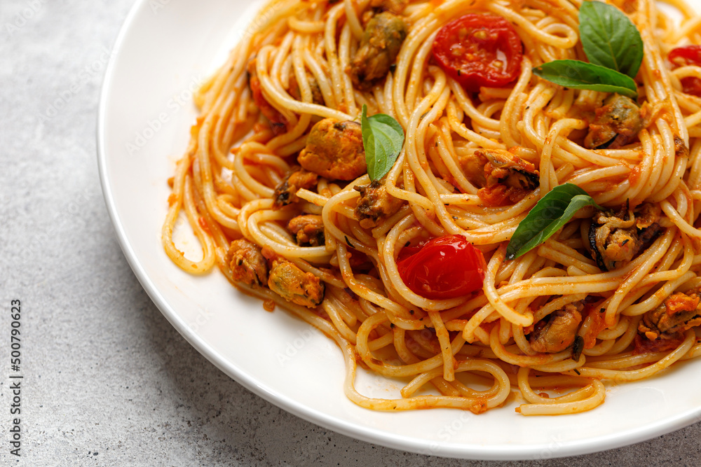 Spaghetti with mussels and tomato cherry sauce in white plate. Close up.