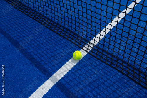 Ball in the shade of the net of a blue paddle tennis court. © Vic