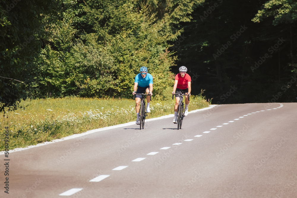 Cyclists couple on the road in summer cycling gear pedaling and gliding positions on racing cycles. Cyclists couple on the road in summer cycling gear pedaling and gliding positions on racing cycles.