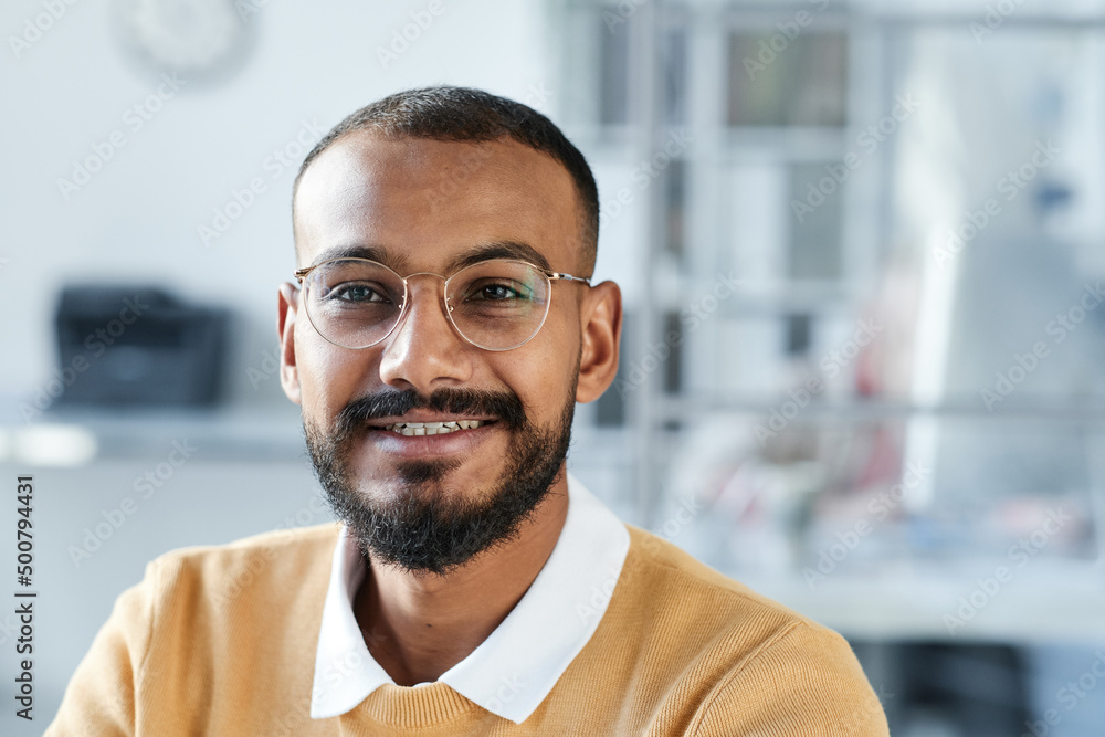 Portrait of smiling handsome young mixed race manager in eyeglasses sitting in contemporary office Portrait of smiling handsome young mixed race manager in eyeglasses sitting in contemporary office