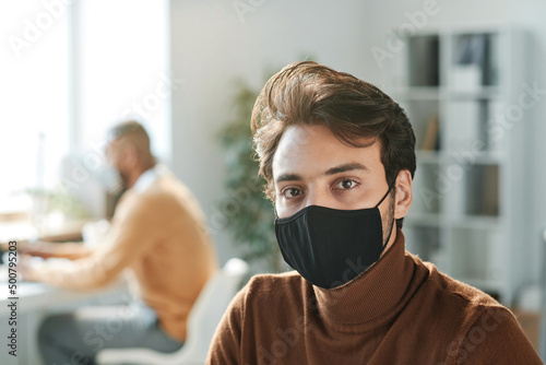 Portrait of young mixed race manager of company with brown hair wearing brown turtleneck and black mask in office