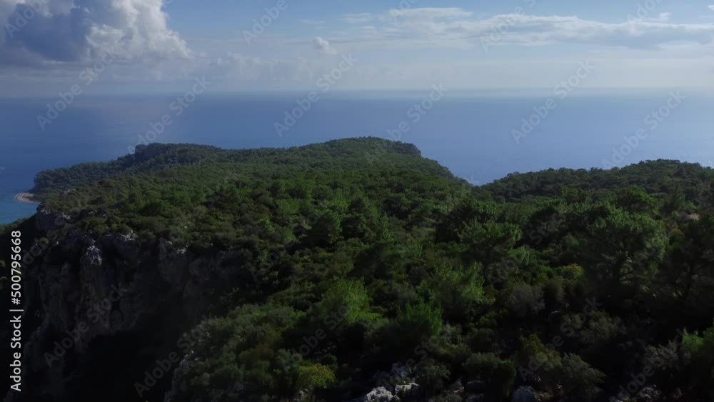 Aerial flight over the green mountains towards Mediterranean coastline at clear summer day. Drone footage of forestry on the cliffs located next to the shore of the blue ocean. Concept of environment. Aerial flight over the green mountains towards Mediterranean coastline at clear summer day. Drone footage of forestry on the cliffs located next to the shore of the blue ocean. Concept of environment.