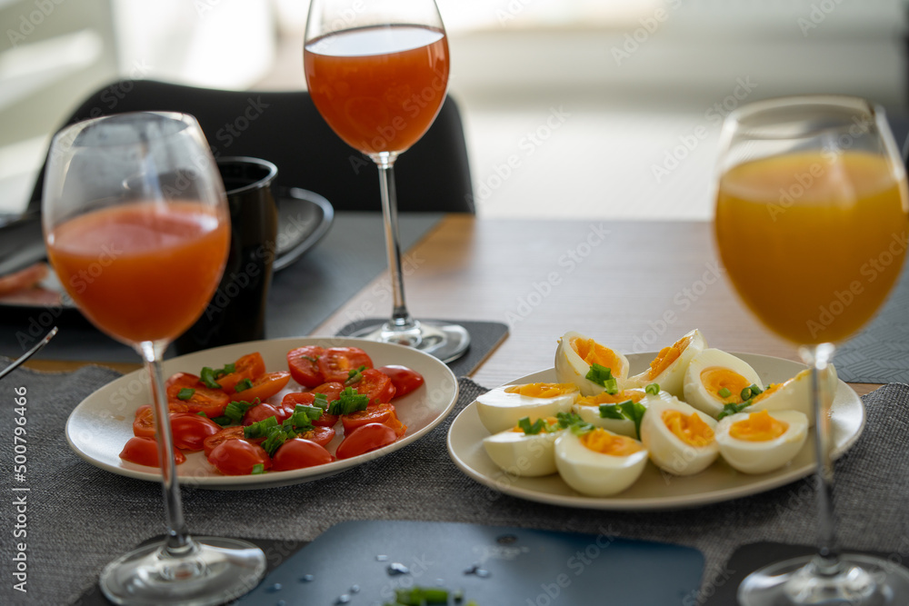 homemade breakfast, yellow cheese with holes, small sliced tomatoes, cottage cheese, egg paste, eggs, chives, tea, orange, carrot and grapefruit juice in wine glasses, black tableware. homemade breakfast, yellow cheese with holes, small sliced tomatoes, cottage cheese, egg paste, eggs, chives, tea, orange, carrot and grapefruit juice in wine glasses, black tableware.