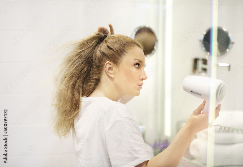 woman in the bathroom drying her hair with a hairdryer woman in the bathroom drying her hair with a hairdryer