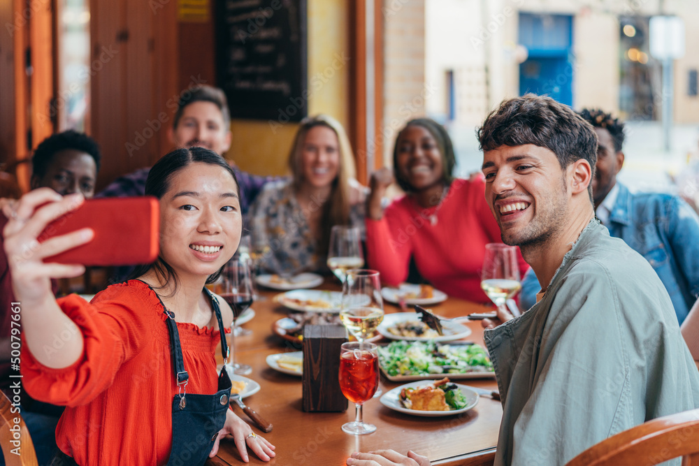 Asian woman taking a selfie at a multiethnic gathering of friends in a restaurant Asian woman taking a selfie at a multiethnic gathering of friends in a restaurant