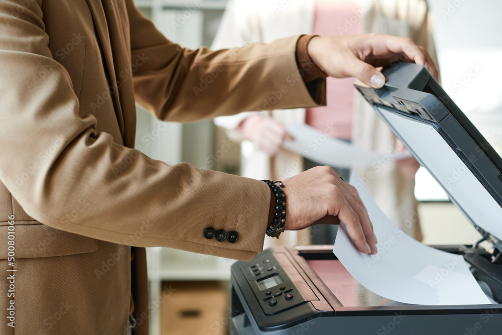 Close-up of unrecognizable man in jacket putting paper into scanner while making copy in office