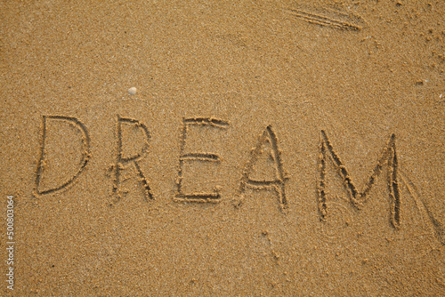 Hand inscribed DREAM on the texture of beach sand. © De Visu