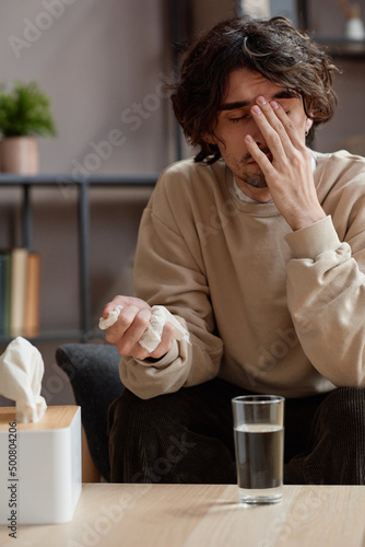Vertical medium portrait of young Caucasian man feeling stressed out having psychologist appointment holding napkin and crying