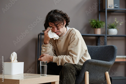 Horizontal medium portrait of despaired young Caucasian man suffering stress having psychologist appointment crying and wiping off tears
