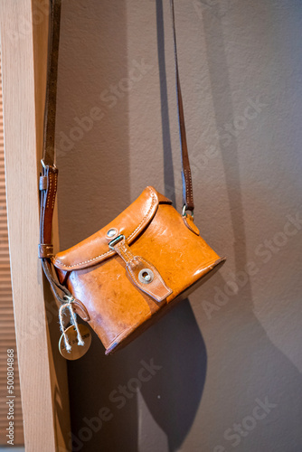 Close-up of stylish yellow leather sling bag. Elegant feminine handbag hanging against wall. Fashionable accessory in empty hotel room.