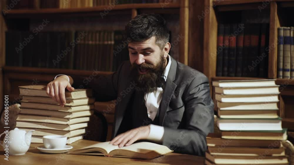 Bearded man in library with books on background. Middle age man reading books at home library. Professor. Bearded man in library with books on background. Middle age man reading books at home library. Professor.