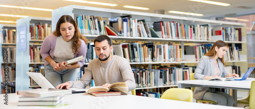 Foto Positive young adults communicating while preparing to exam in library