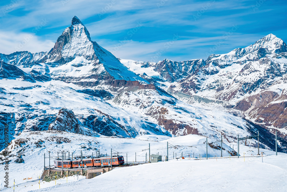 View of red train climbing up to gornergrat station. Scenic view of matterhorn mountain against sky. Famous tourist place in alpine region.