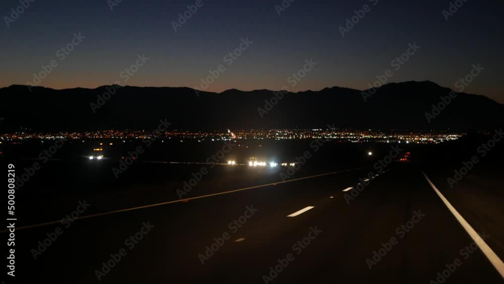 Car driving on desert road at night, freeway or highway in twilight dusk, perspective view thru windscreen or windshield. Road trip in California USA. Valley and mountains on horizon, dividing line. Car driving on desert road at night, freeway or highway in twilight dusk, perspective view thru windscreen or windshield. Road trip in California USA. Valley and mountains on horizon, dividing line.