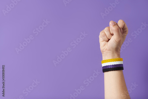 Fotografi Raised fist of a person wearing a non binary flag bracelet