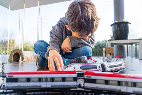 Young kid playing with toy trains on the floor. Toy train similar to Cercanias Renfe Spanish train and Ave high speed train