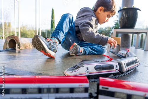 Young kid playing with toy trains on the floor. Toy train similar to Cercanias Renfe Spanish train and Ave high speed train