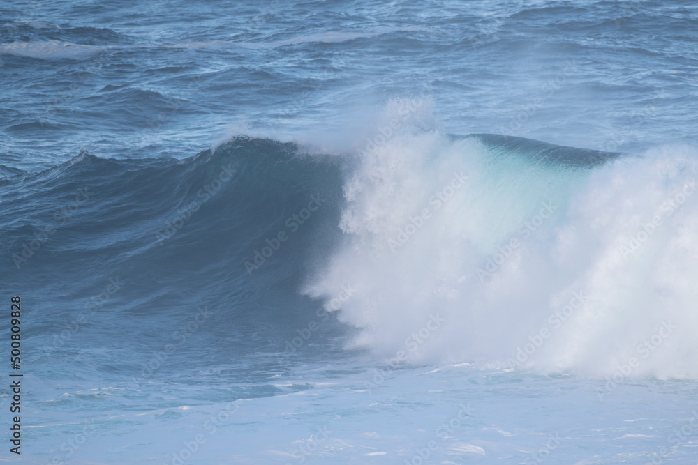 An angry turquoise green color massive rip curl of a wave as it barrels rolls along the ocean. The white mist and froth from the wave are foamy and fluffy. The ocean in the background is deep blue. An angry turquoise green color massive rip curl of a wave as it barrels rolls along the ocean. The white mist and froth from the wave are foamy and fluffy. The ocean in the background is deep blue.