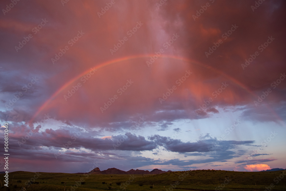 Rainbow at sunset over grasslands and mountains
