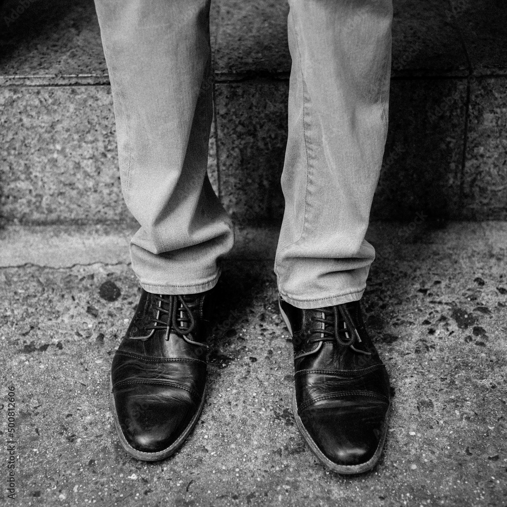 Man's legs and feet wearing cap toe shoes outside a doorstep on a New York City street. Black