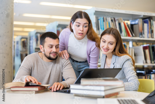 Friendly group of students is preparing for classes on a laptop, studying in the university library