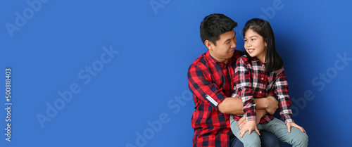 Happy Asian man and his little daughter on blue background with space for text