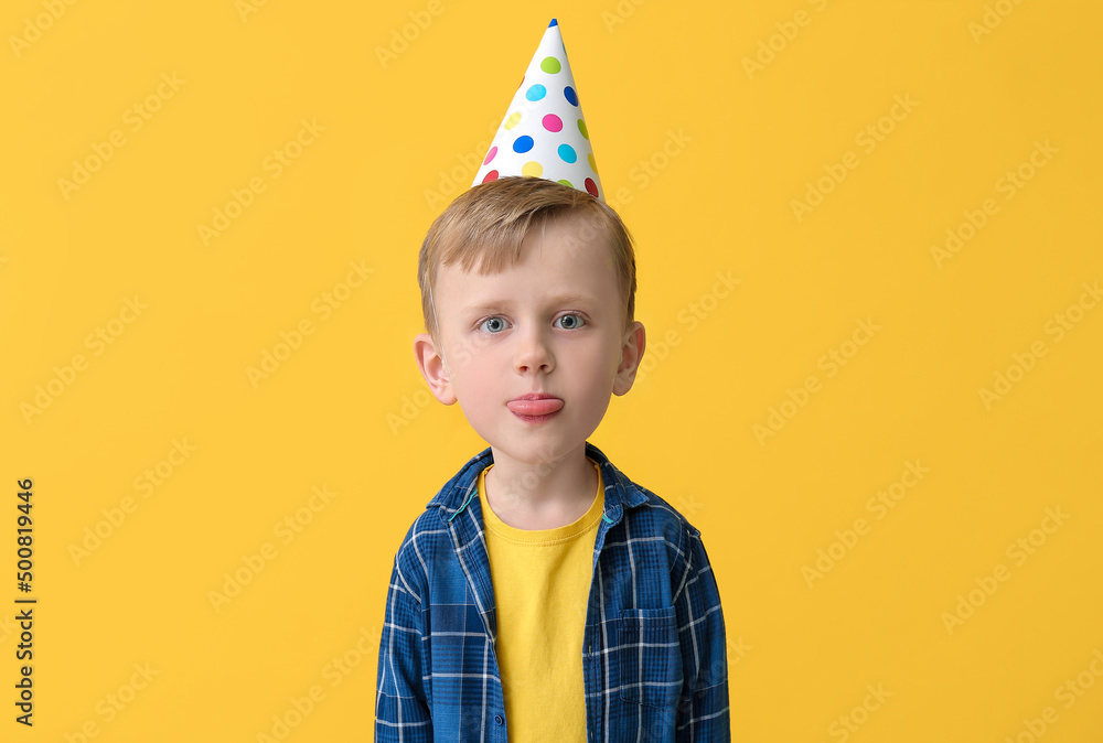 Funny little boy with big head wearing Birthday hat and showing tongue on color background Funny little boy with big head wearing Birthday hat and showing tongue on color background