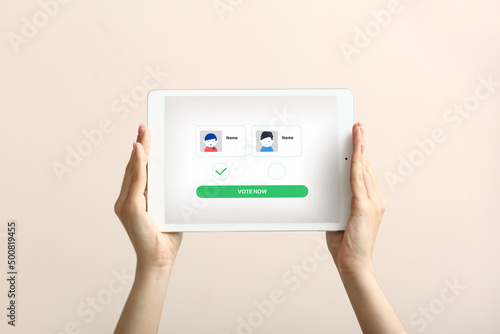 Female hands holding tablet computer with text VOTE NOW and icons of candidates on screen against light background