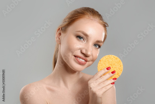 Beautiful woman with makeup sponge on grey background photo