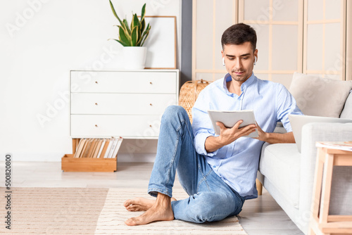 Young barefooted man reading magazine at home