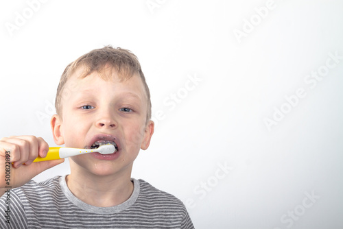 A Caucasian boy in a gray T-shirt brushes his teeth with a black charcoal toothpaste