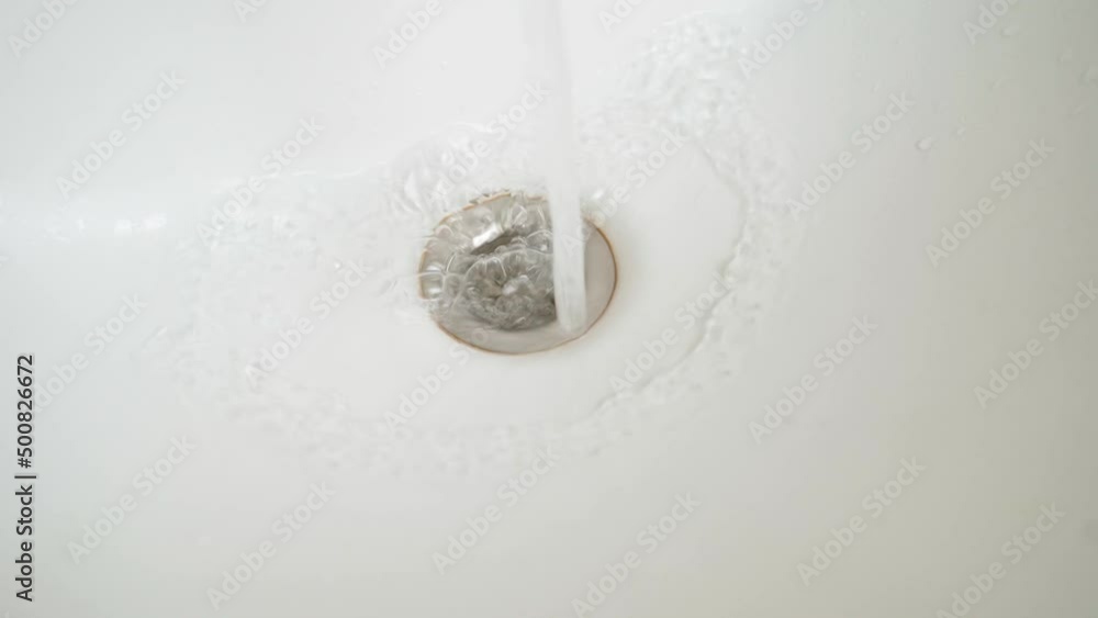 Water flows into the drain hole of a white bathroom close-up Water flows into the drain hole of a white bathroom close-up