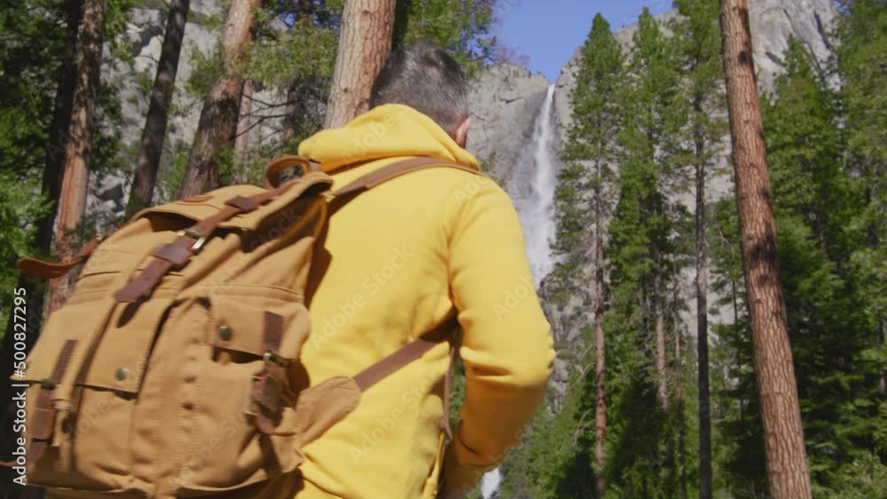 White male hiking on trail up peaceful high elevation with Yosemite waterfall 