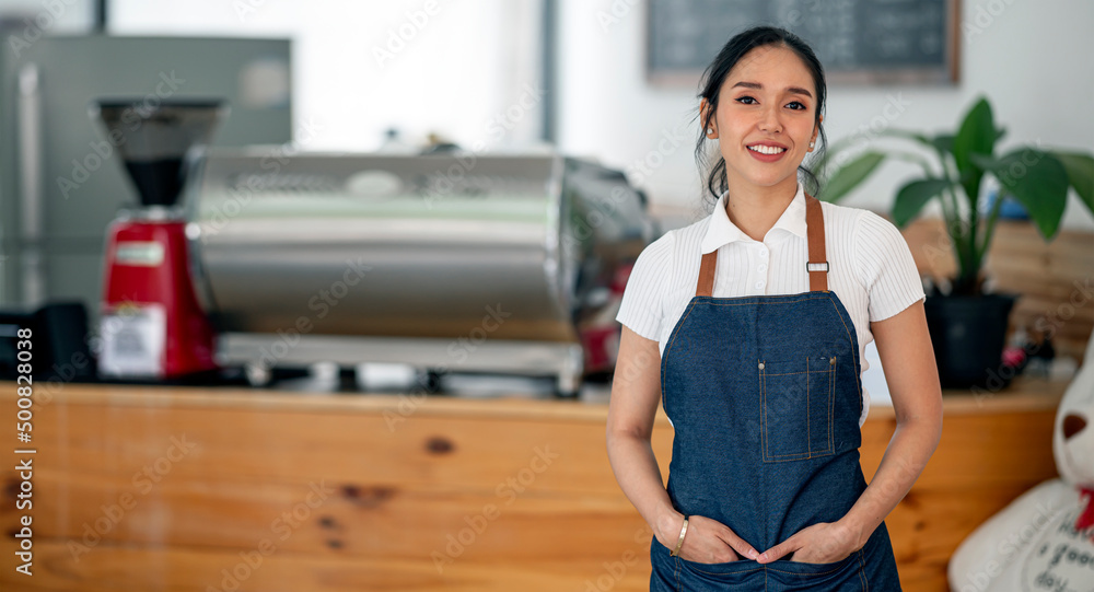 Smiling young asian female barista in apron standing in her cafe. Smiling young asian female barista in apron standing in her cafe.