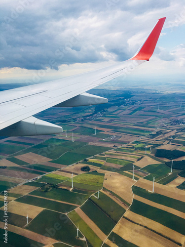 Beautiful view from the window on the wing of the aircraft and the multi-colored landscape of Austria. The plane flies below the clouds over the fields of Austria. Vertical. Vienna, Austria