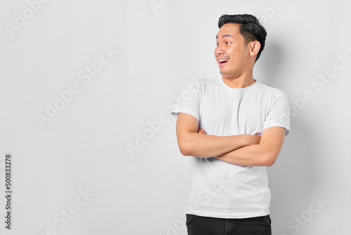 Portrait of amazed young Asian man crossed arms and looking aside at blank space isolated on white background