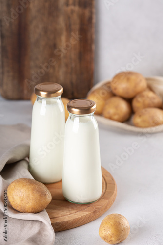 Bottles with vegan plant based milk. Dairy-free drink and potato tubers on gray table