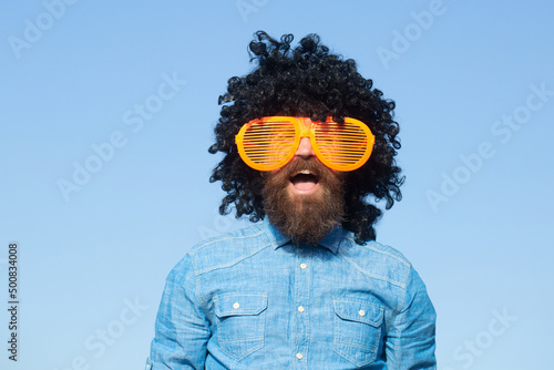 Fototapeta Crazy funny bearded man with wig and fun glasses on sky background