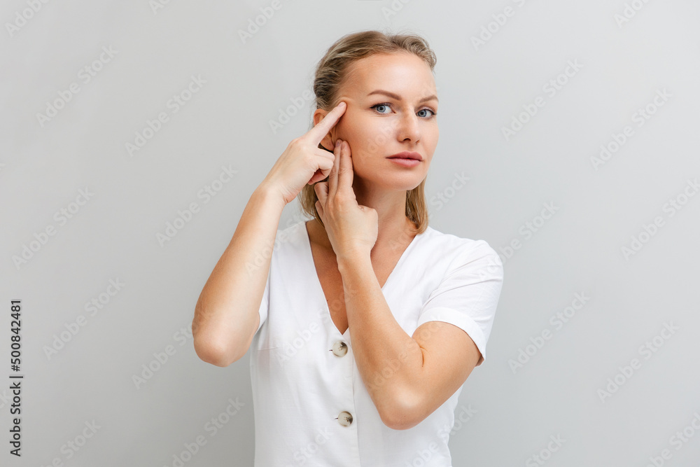 Portrait of a young beautiful woman, pulling the skin on her temples with her fingers. Gray background. The concept of aging and facial wrinkles Portrait of a young beautiful woman, pulling the skin on her temples with her fingers. Gray background. The concept of aging and facial wrinkles